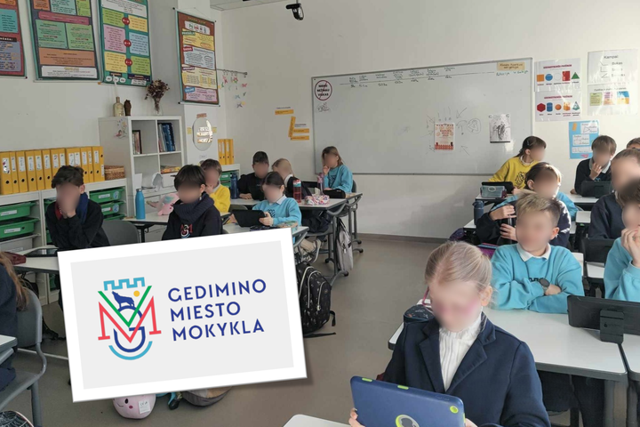 Mokyklos klasėje, Gedimino miesto mokykloje, mokiniai apsirengia įvairiais rūbais sėdi prie stalų ir dirba su planšetėmis. Klasės sienos papuoštos įvairiais mokomaisiais plakatais ir lentomis. Į klasę skleidžiasi dienos šviesa.