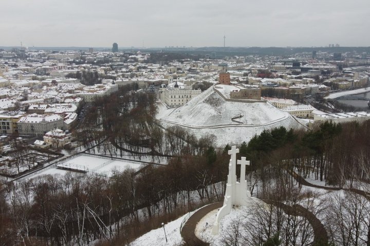 Žiemos peizažas iš paukščio skrydžio Vilniuje. Priekyje matomas Trijų Kryžių paminklas stovintis ant kalvos apsuptos medžių. Fone iškilęs Gedimino pilies bokštas ant snieguoto Gedimino kalno, o tolumoje matosi senamiesčio stogai, upė Neris ir Televizijos