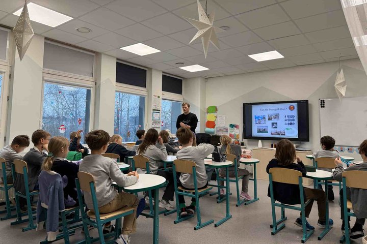 Nuotraukoje matome klasę, kurioje prie suolų sėdi šešiolika pradinukų. Septynios mergaitės ir devyni berniukai. Ant keletas suolų yra padėti penalai, tačiau kai kurie suolai tušti. Klasė yra papuošta žemėlapiu, tvarkaraščiu ir knygų nuotraukomis. Ant sien