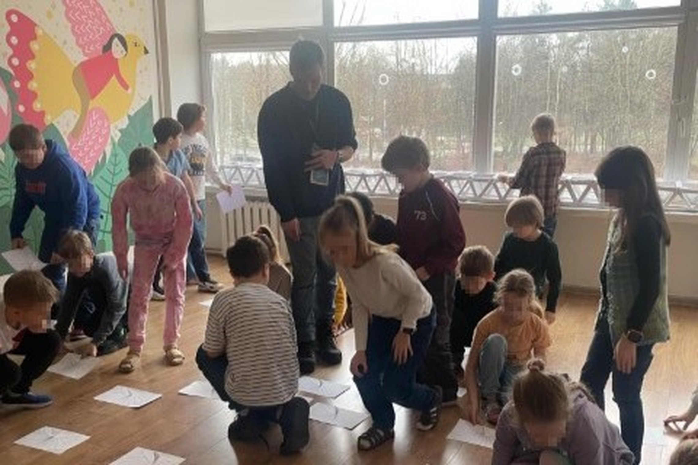 Vaizduojama mokyklos klasė, pilna vaikų. Daugelis atsistoję arba pritūpę prie ant grindų išdėliotų popieriaus lapų su vertikaliai priklijuotais kartono gabalėliais, tai vaikų pagaminti saulės laikrodžių modeliukai. Jie išdėlioti priešais didelius langus k