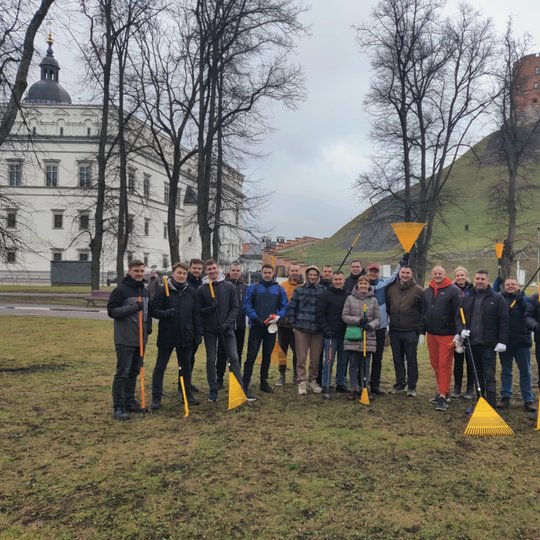 Priešais Gedimino pilies kalną ir Valdovų rūmus Vilniuje stovi grupė žmonių, pasiryžusių talkai – jie rankose laiko geltonus grėblius ir vilki šiltais drabužiais. Fone matyti žalios kalvos šlaitas su Gedimino pilies bokštu viršuje ir žiemos pradžios oras