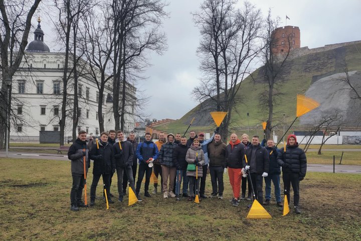 Priešais Gedimino pilies kalną ir Valdovų rūmus Vilniuje stovi grupė žmonių, pasiryžusių talkai – jie rankose laiko geltonus grėblius ir vilki šiltais drabužiais. Fone matyti žalios kalvos šlaitas su Gedimino pilies bokštu viršuje ir žiemos pradžios oras 