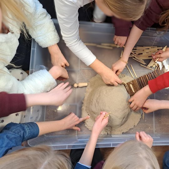 Pradinukai iš Filaretų mokyklos statydina piliakalnio modelį smėlyje, naudodami medinius pagaliukus ir žmogeliukų figūrėles; edukacijos metu mokiniai praktiškai susipažįsta su senovės įtvirtinimų sandara.