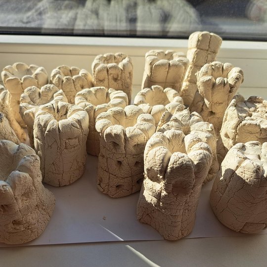 Iš molio nulipdyti, saulėje džiūstantys cilindro formos Gedimino bokštai, sustatyti ant balto popieriaus lapo prie lango.