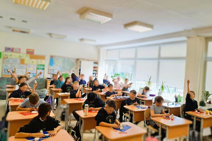 Būrelis berniukų stovi priešais klasės ekraną, kuriame rodomas Gediminaičių dinastijos genealoginis medis su pagrindinių valdovų vardais ir paveldimumo ryšiais; šalia pateiktas paaiškinimas, kas yra dinastija. Vaikai dėvi kasdienius drabužius, o foną papi