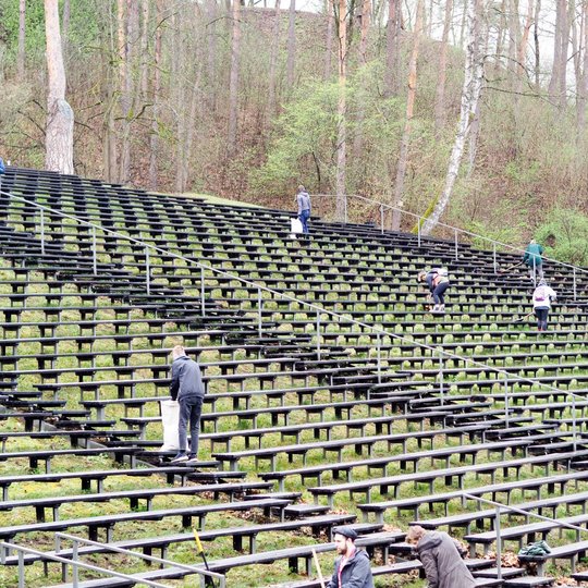 Lauko estradoje, įrengtoje ant miškingo šlaito, gausus žmonių būrys darbuojasi – valo tarp suolų susikaupusius lapus, renka šiukšles į baltus maišus. Talkininkai išsidėstę per visą suoliukų plotą, kai kurie lenkiasi, kiti naudoja įrankius.