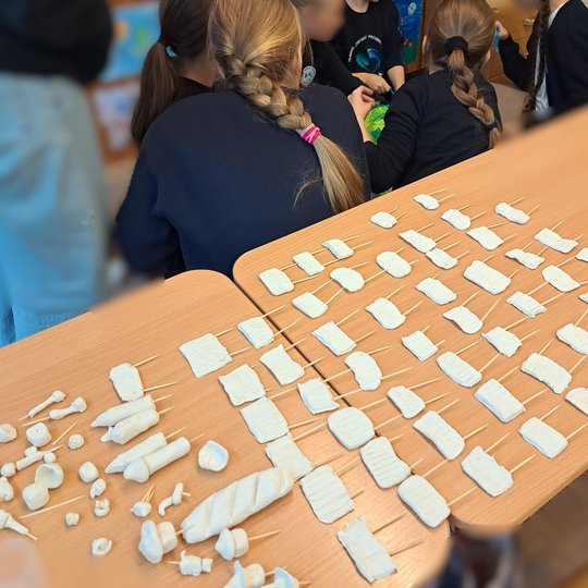 Nuotraukoje stalas pilnas pilies elementų - tvoros, bokštai, sienos. Aplinkui vaikai.