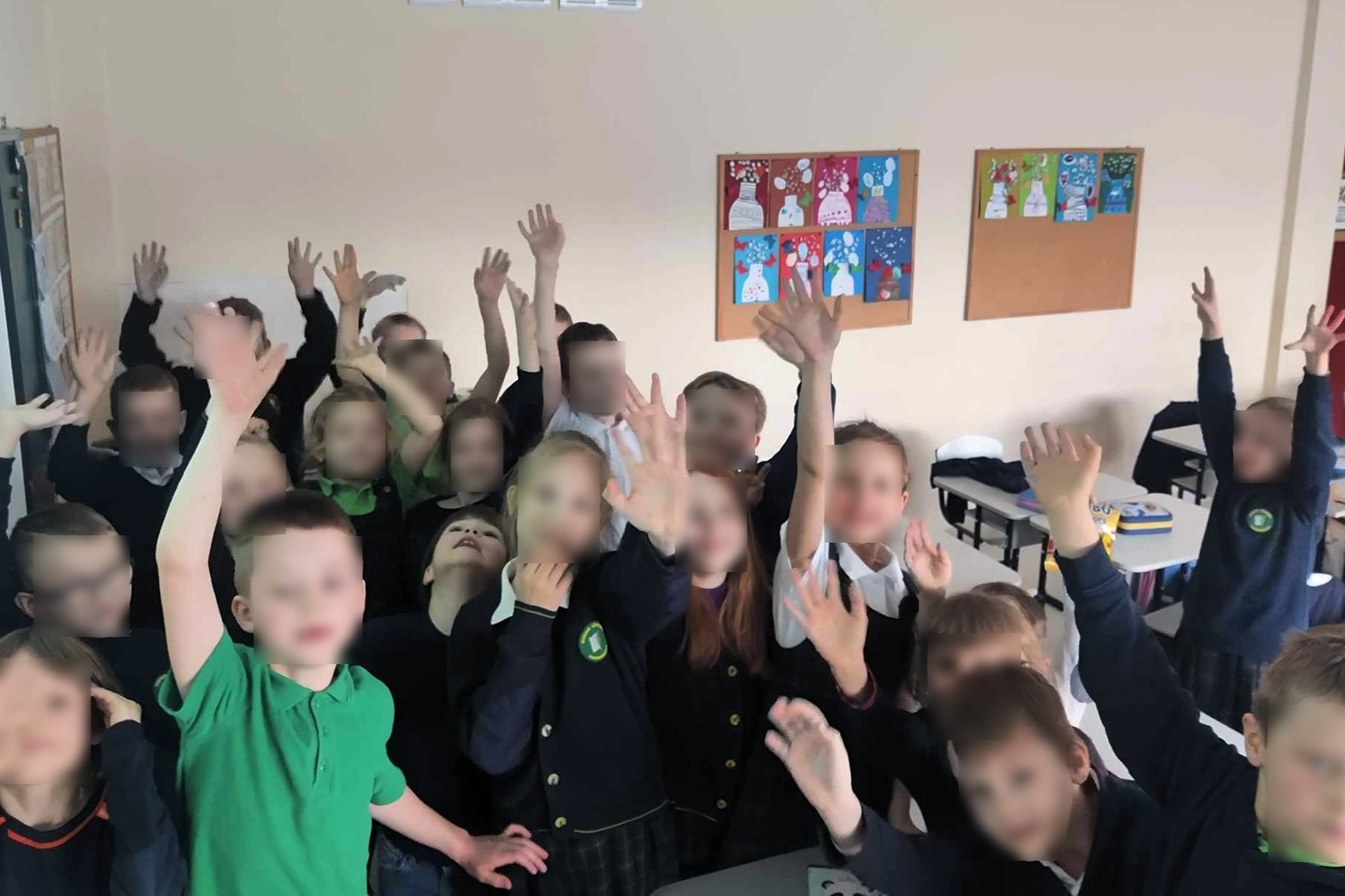 Laimingi Ąžuolyno progimnazijos mokiniai klasėje, šypsenomis ir pakeltomis rankomis reiškiantys džiaugsmą po įkvepiančios pamokos. Ant sienos kabantys spalvoti piešiniai su žiemos motyvais prideda jaukumo jų klasės aplinkai.