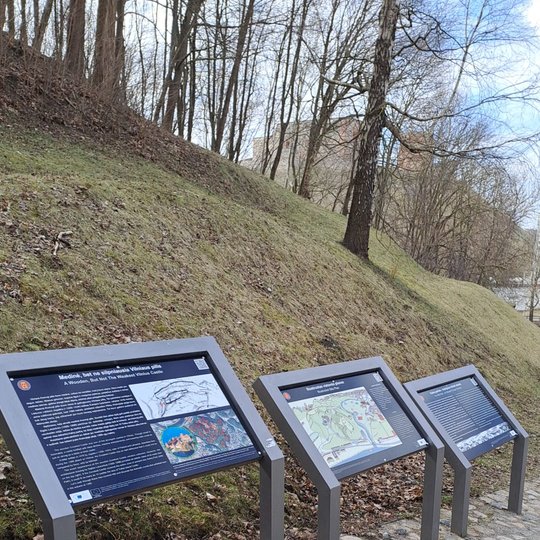 Trys informaciniai stendai Vilniaus pilių teritorijoje, išdėstyti palei taką ant kalno šlaito. Pirmasis stendas pristato medinę, bet ne silpnąją Vilniaus pilį, antrasis – Kreivosios pilies planą, o trečiasis – pilių rekonstrukciją. Fone matyti medžių kami