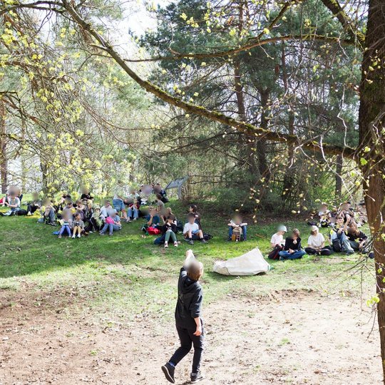 Grupė vaikų sėdi ant žolės miško pievoje, ilsisi pavėsyje po medžiais. Priekyje vaikas eina link jų, pakėlęs ranką. Aplink – pavasarinė žaluma.