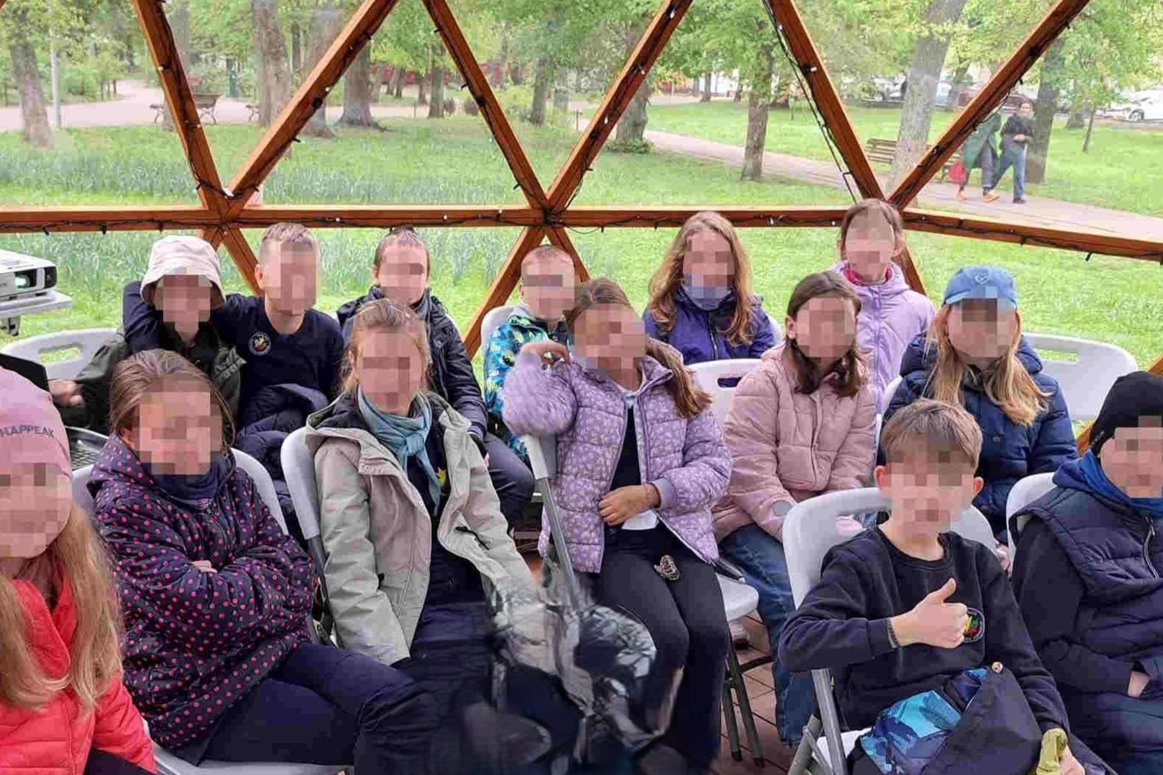 Grupė vaikų sėdi kupolo formos palapinėje lauko aplinkoje, dėmesingai klausosi edukacijos apie „Roko maršą“ Vilniaus pilyse.