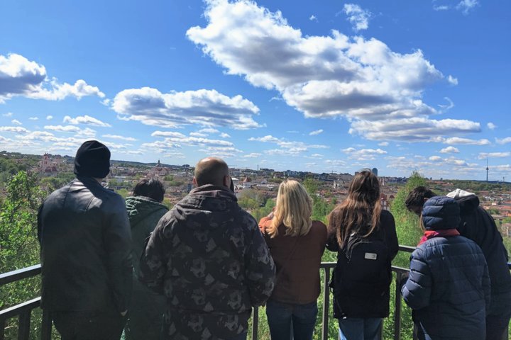 Ekskursijos dalyviai stebi Vilniaus senamiesčio panoramą nuo kalvos – matomi miesto bažnyčių bokštai, senamiesčio stogai ir tolumoje Vilniaus televizijos bokštas.