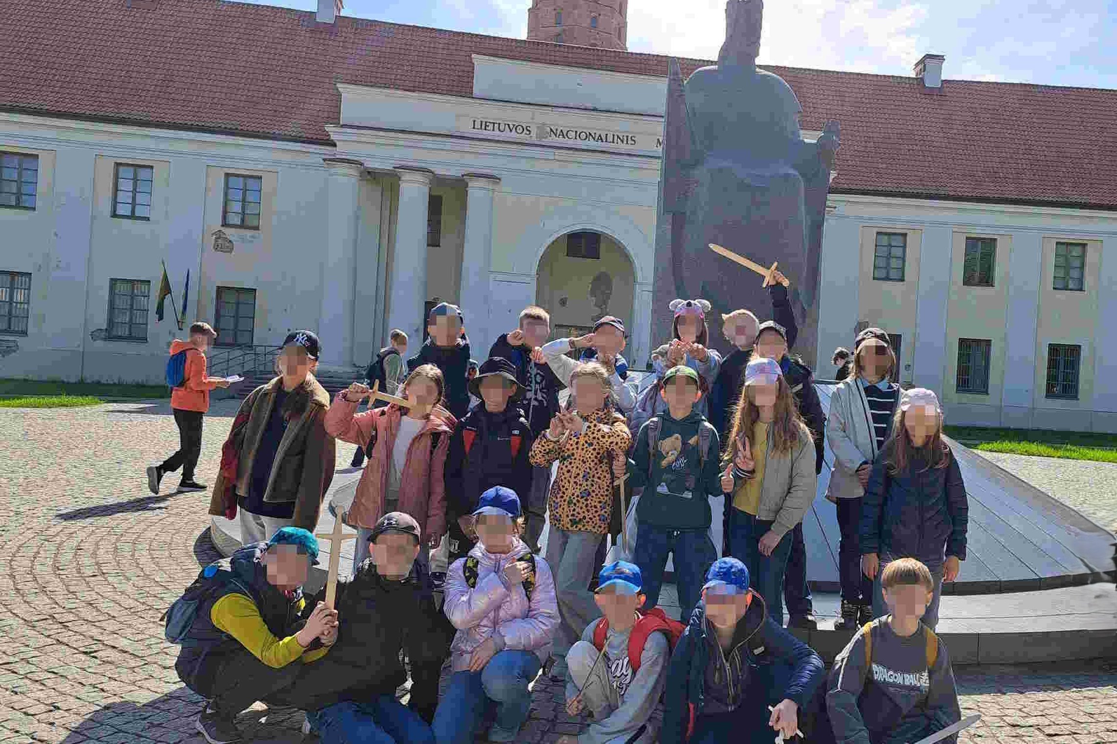 Pradinukai po edukacijos „Gediminas ir trys Vilniaus pilys“ pozavo prie kunigaikščio Mindaugo paminklo Vilniuje. Vaikai linksmai nusiteikę laiko rankose medinius kalavijus ir istorinių herojų atributiką.
