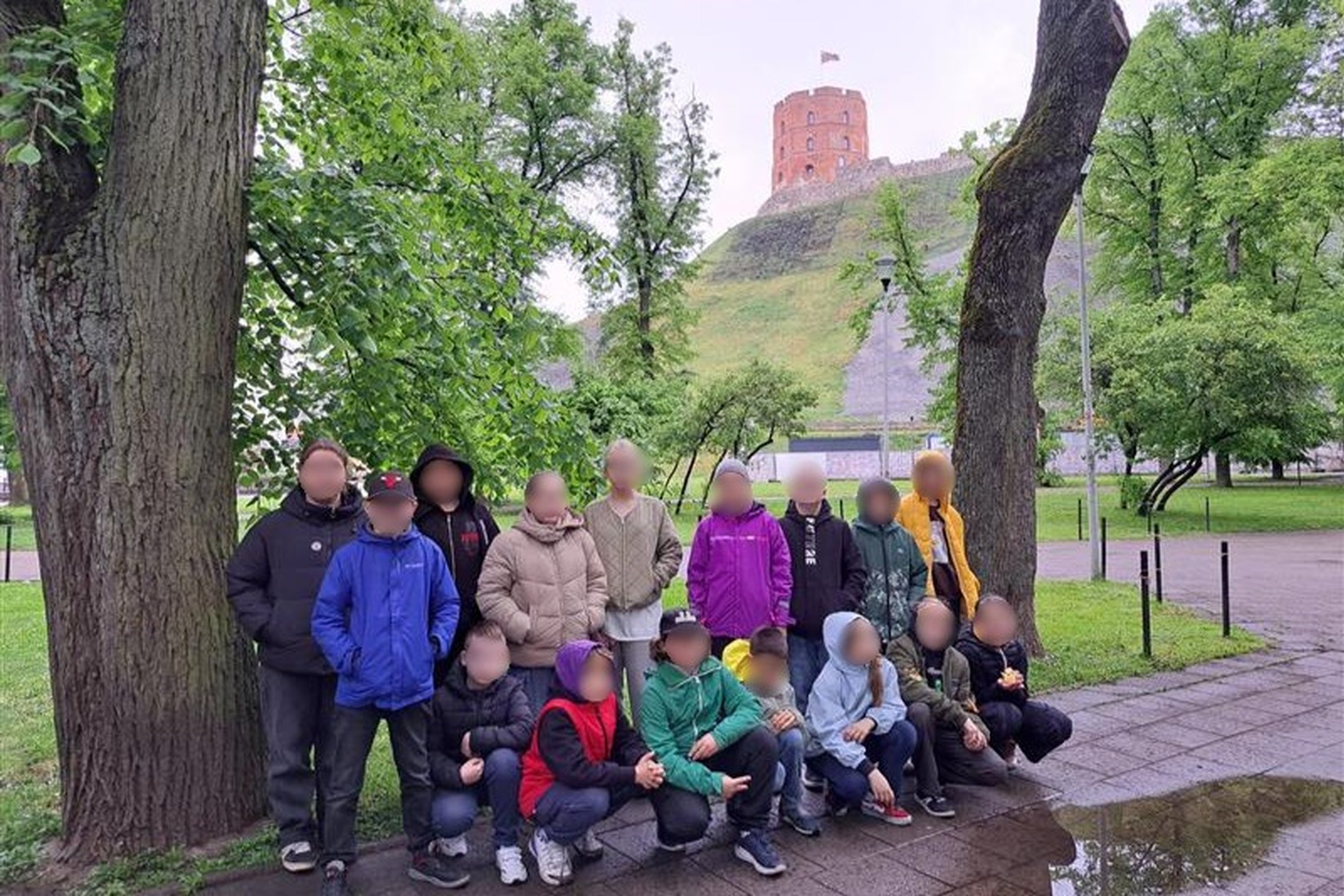 Nuotraukoje matoma grupė vaikų, pozuojančių prie Gedimino pilies kalno Vilniuje. Jie stovi žalioje aplinkoje, tarp medžių, o fone matyti garsioji Gedimino pilies bokšto viršūnė su plevėsuojančia Lietuvos vėliava. Vaikai apsirengę šilčiau – dėvi striukes, 