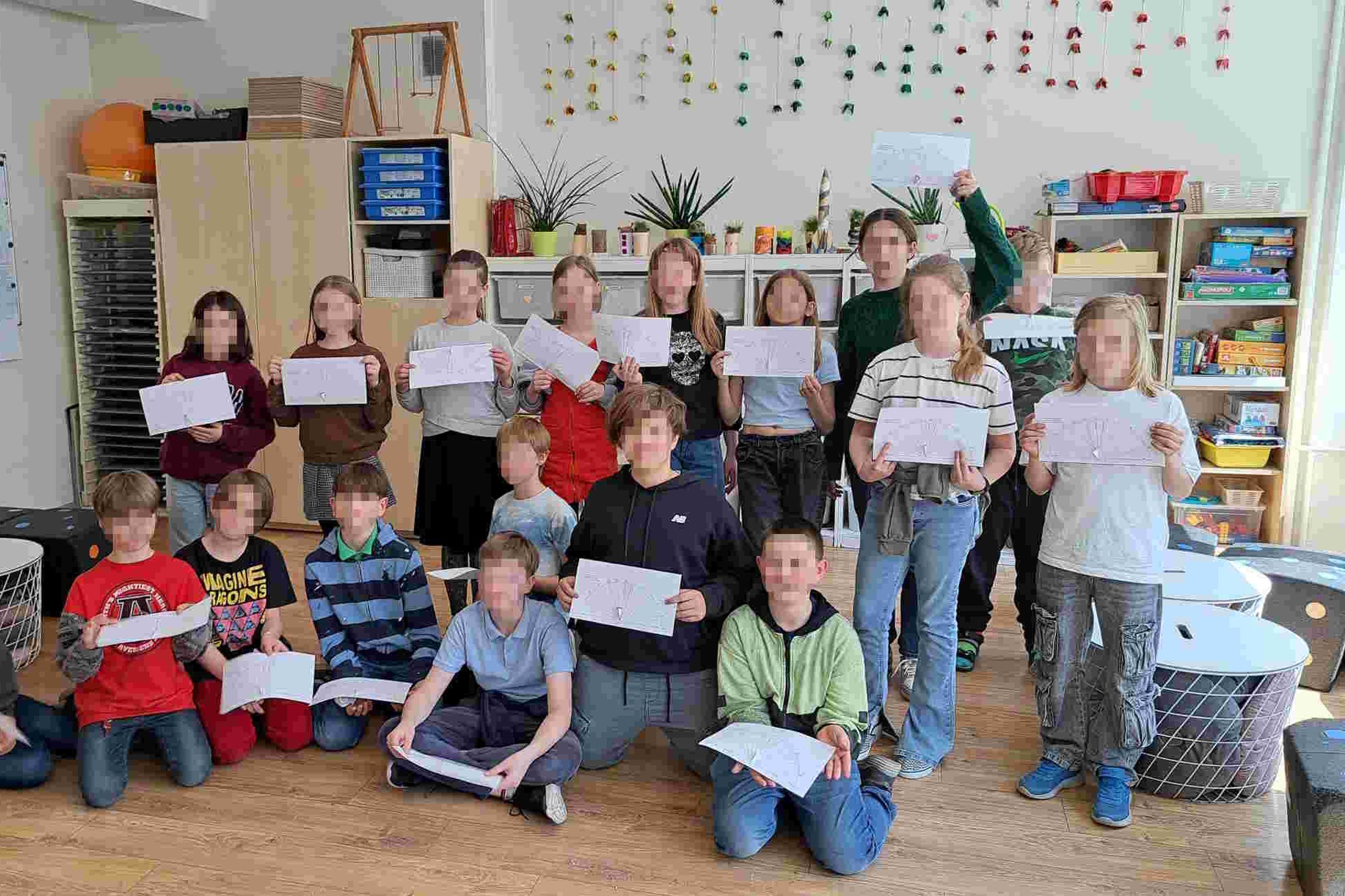 ChatGPT said: Ketvirtokai klasėje po edukacijos laiko rankose pasigamintus saulės laikrodžių brėžinius. Vaikai pozuoja bendrai nuotraukai apsupti mokyklinių priemonių ir žaidimų lentynų.