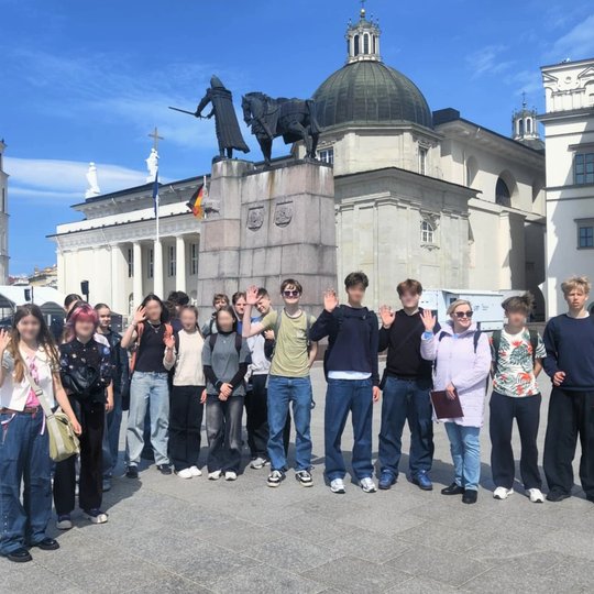 Grupė paauglių mokinių ir jų mokytoja stovi Katedros aikštėje Vilniuje priešais Lietuvos valdovo Gedimino paminklą, iškilusį ant aukšto postamento. Paminklas vaizduoja kunigaikštį Gediminą stovintį šalia žirgo, su pakelta dešine ranka, laikydamas kalaviją