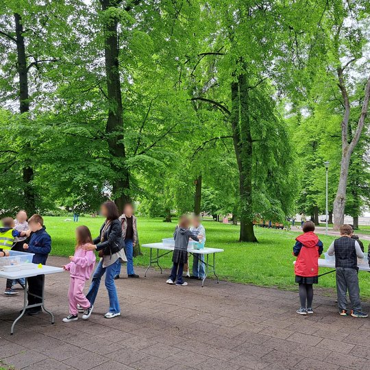 Nuotraukoje – edukacinė veikla vykstanti lauke, Vilniaus pilių teritorijoje, prie pat Gedimino pilies kalno. Vaikai, vilkintys ryškiaspalves liemenes, dirba mažomis grupelėmis prie stalų, kur atlieka kūrybinę užduotį – statyti piliakalnių modelius. Kiekvi