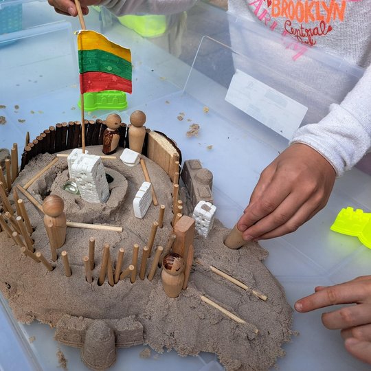 Nuotraukoje akcentuojamos vaikų sukurtos piliakalnių miniatiūros – su gynybinėmis sienomis, vartais, pastatais ir Lietuvos trispalve, iškeltą centrinėje konstrukcijos dalyje. Šie darbeliai liudija ne tik apie kūrybiškumą, bet ir apie pagarbą Lietuvos isto
