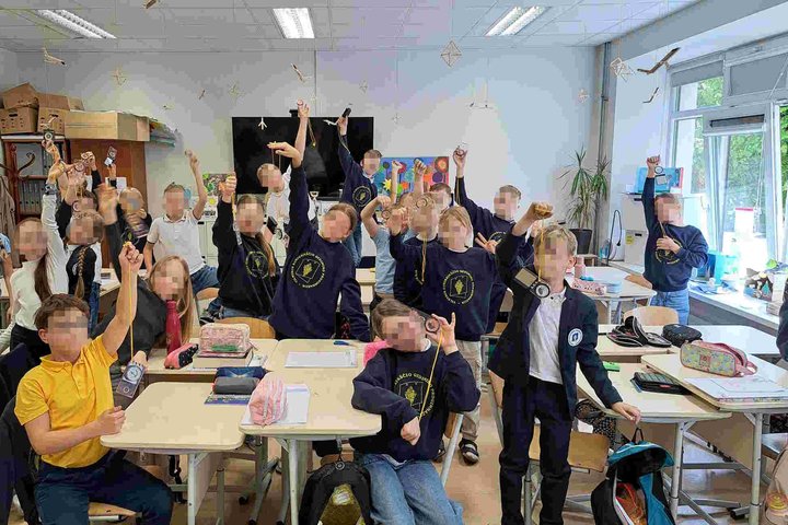 Trečiokai klasėje linksmai laiko rankose kompasus po edukacinio užsiėmimo. Ant vaikų uniformų matyti Vilniaus kunigaikščio Gedimino progimnazijos ženklai.