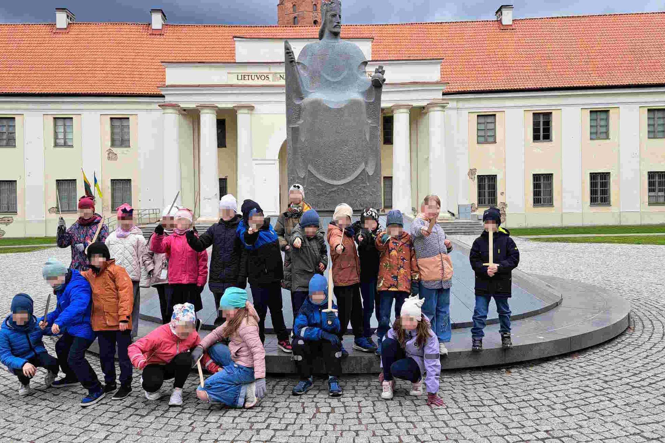 Grupė vaikų pozuoja priešais Mindaugo paminklą prie Lietuvos nacionalinio muziejaus pastato su kolonada Vilniuje.