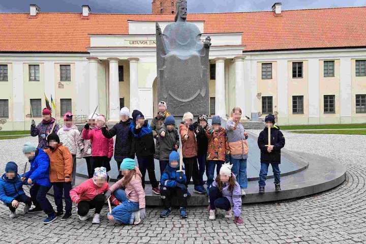 Grupė vaikų pozuoja priešais Mindaugo paminklą prie Lietuvos nacionalinio muziejaus pastato su kolonada Vilniuje.