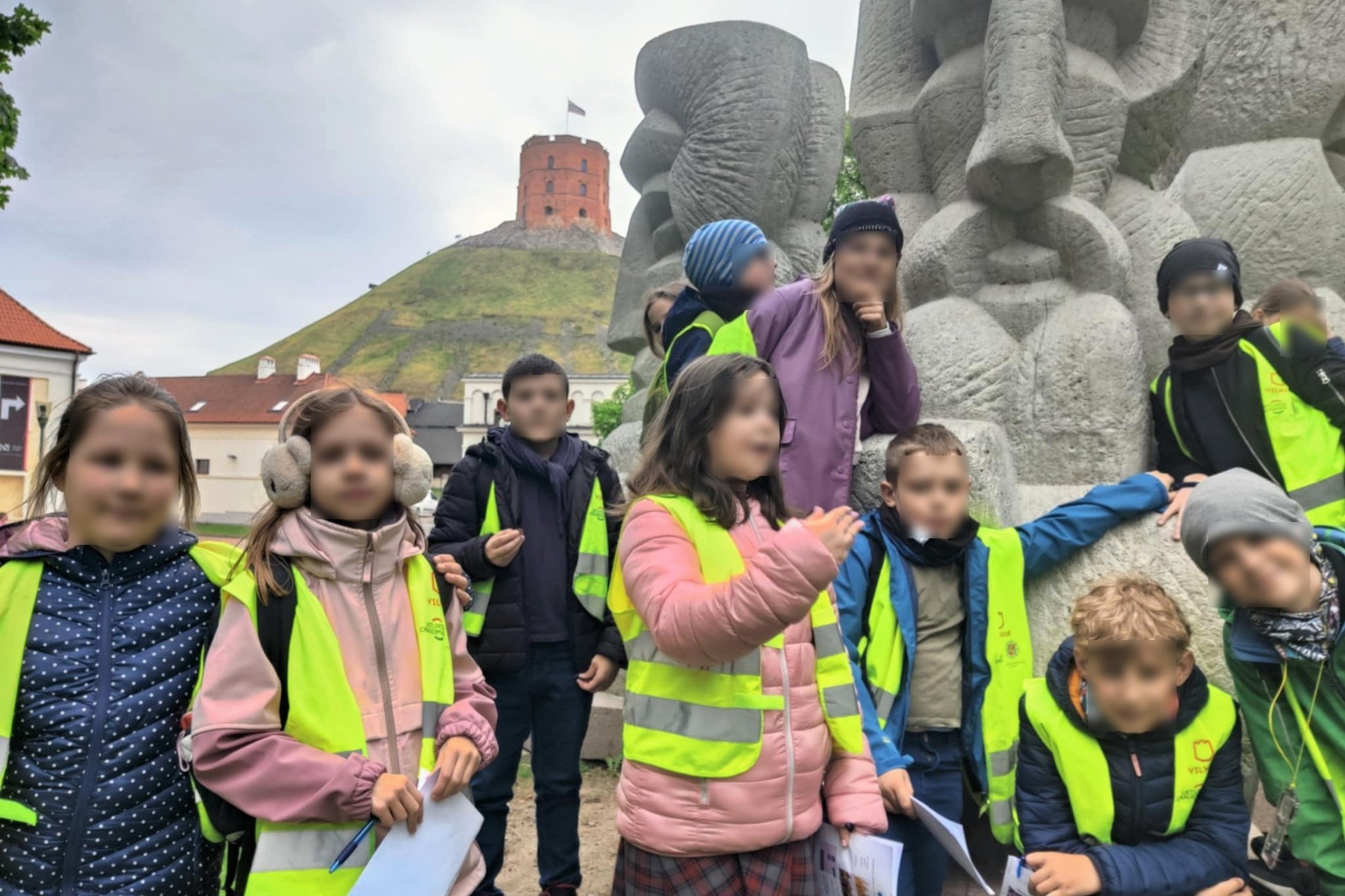 Nuotraukoje matyti vaikų grupė, apsirengusi ryškiaspalvėmis liemenėmis, stovinti prie Vlado Vildžiūno paminklo „Trys karaliai“, kuris vaizduoja simbolinę Lietuvos didžiųjų kunigaikščių genealogiją. Fone aiškiai matomas Gedimino pilies bokštas ant Gedimino