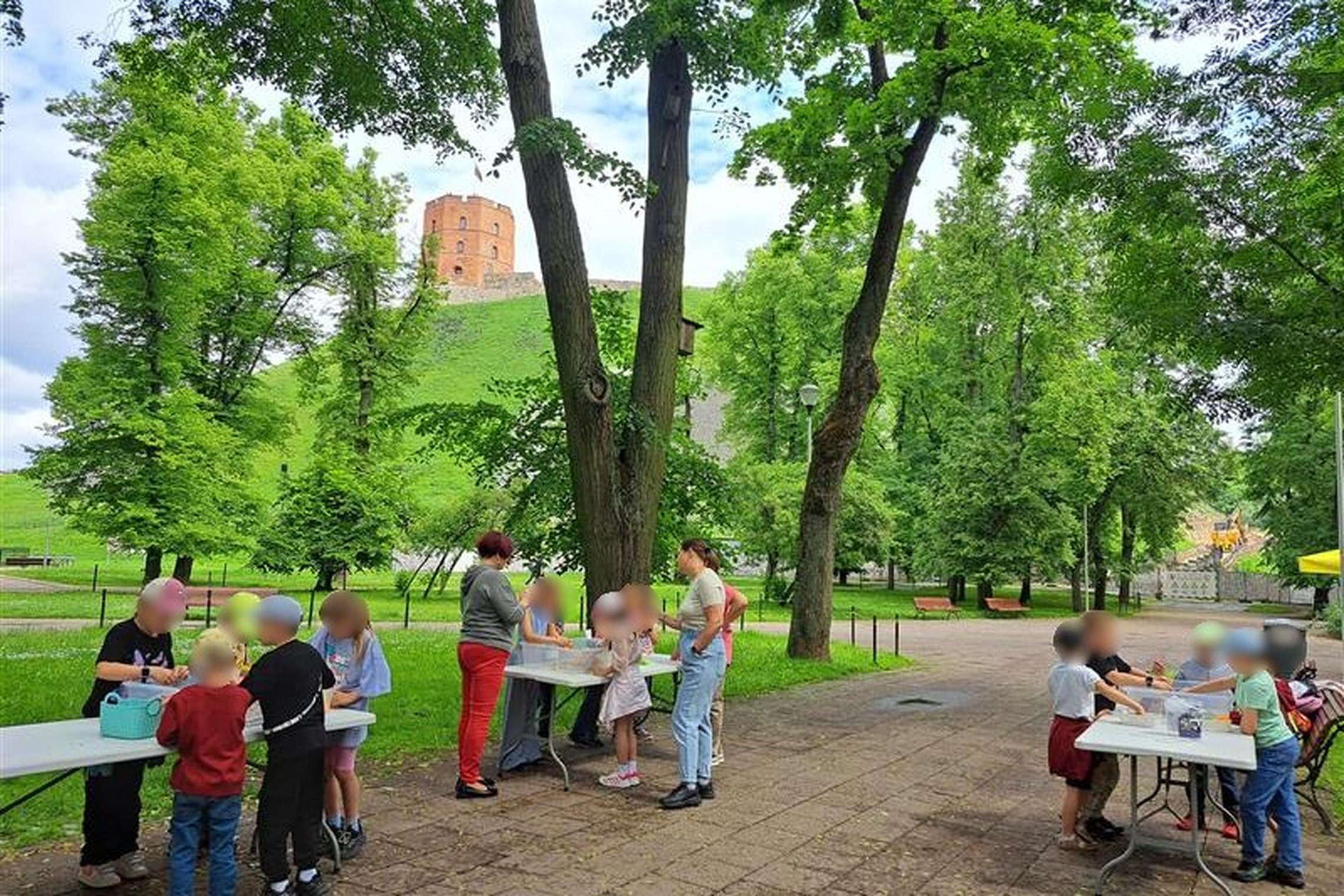 Nuotraukoje vaikai prie stalų stato piliakalnius. Veiksmas vyksta Gedimino pilies kalno papėdėje