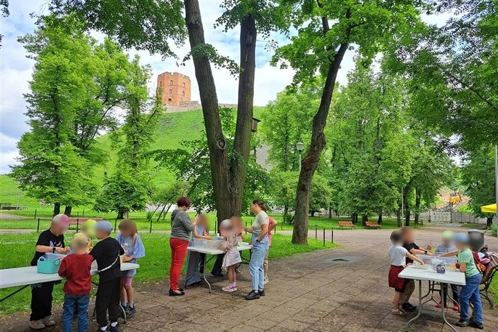 Nuotraukoje vaikai prie stalų stato piliakalnius. Veiksmas vyksta Gedimino pilies kalno papėdėje