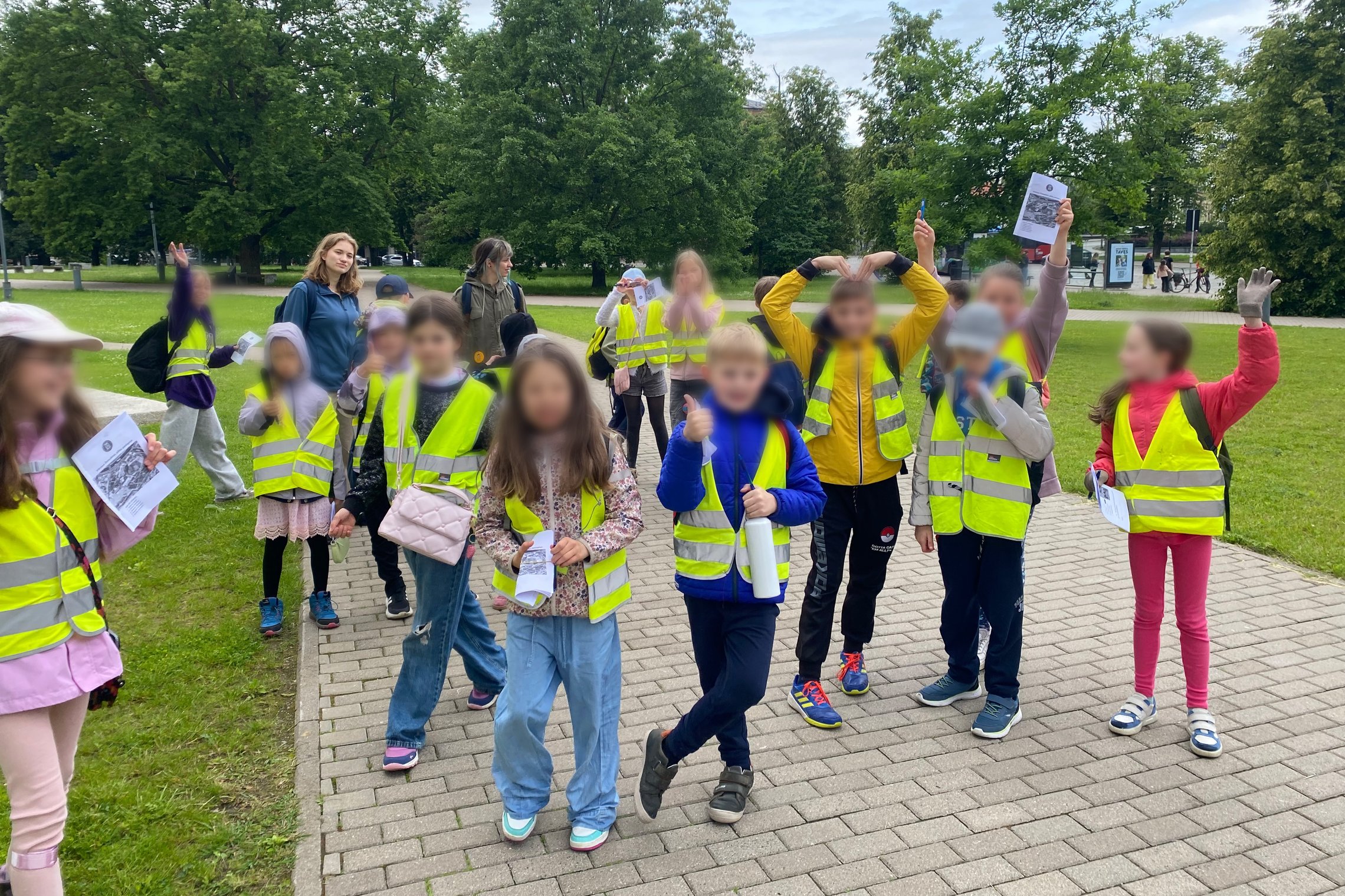 Grupė pradinių klasių mokinių lauke po edukacinės veiklos su džiaugsmu rodo atliktas užduotis