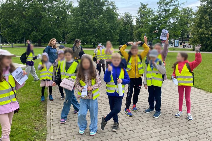 Grupė pradinių klasių mokinių lauke po edukacinės veiklos su džiaugsmu rodo atliktas užduotis