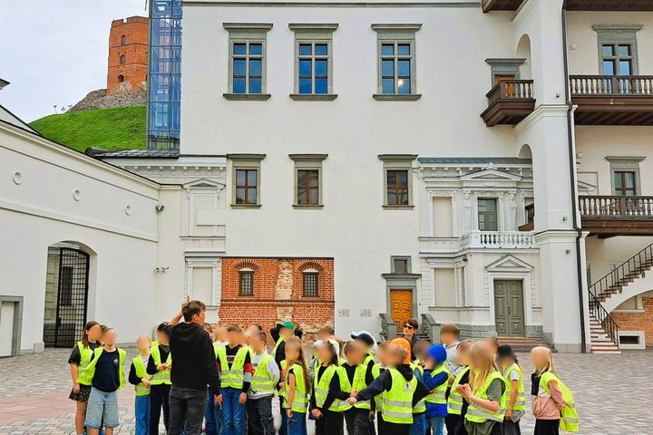 Nuotraukoje vaikai klausosi gido. Už jų Gedimino pilies bokštas.
