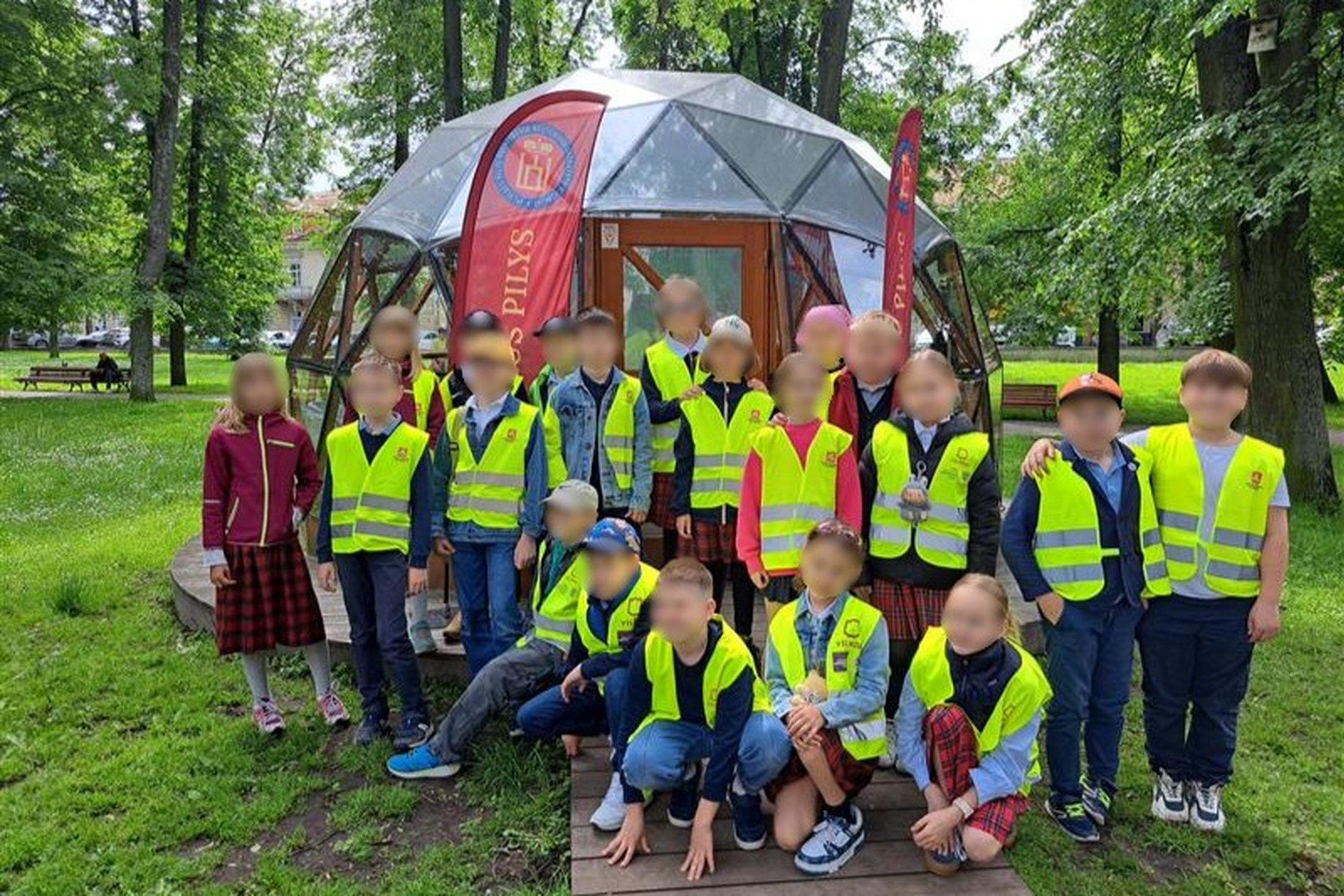 Nuotraukoje grupė vaikų, pozuoja prie Vilniaus pilių kupolo. 