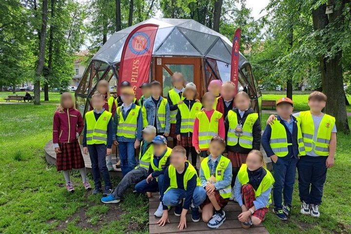Nuotraukoje grupė vaikų, pozuoja prie Vilniaus pilių kupolo. 