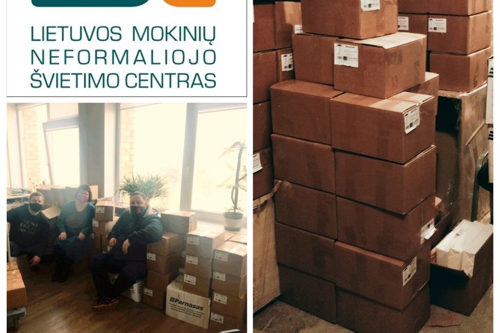 Sudėtos dėžės su knygomis. Paruoštos išvežti iš sandelio. Kitoje nuotraukos dalyje sėdi ant kėdžių žmonės, o šalia jų padėtos knygos dėžėse.