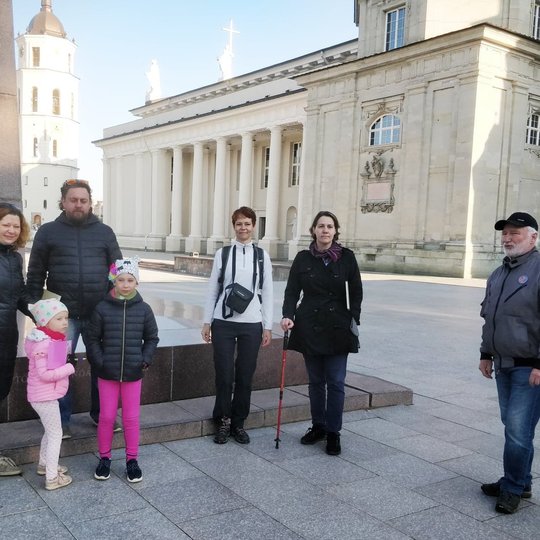 Į pažintinę ekskursiję atėjo tėveliai su vaikais. Ankstus rytas. Jie stovi prie Gedimino paminklo.