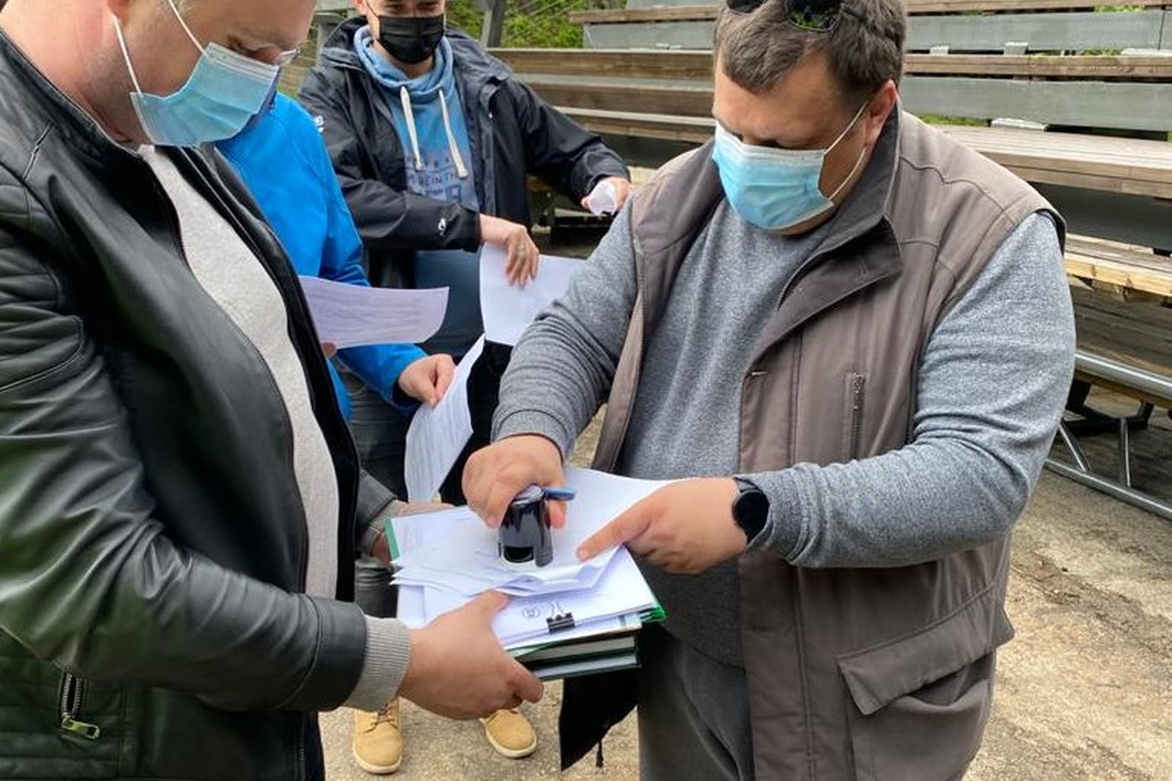 Stovi keturi vyrai. Jie su kaukėmis, rankose dokumentai, yra dedamas antspaudas - pasirašomi Dainų estrados remonto darbų priėmimo aktai. Už vyrų nugarų - nauji estrados mediniai suoliukai.