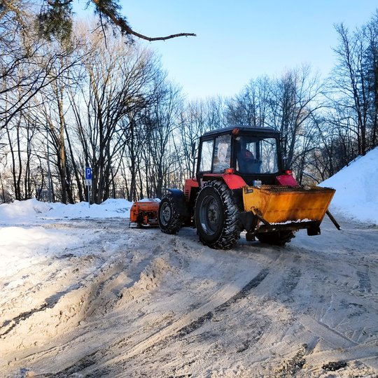 Galingas traktorius kasa sniegą mašinų stovėjimo aikštelėje. Taip pat aikštelę barsto smėliu. Yra giedra, šalta diena.