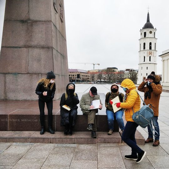Grupė paukščių stebėtojų renkasi prie Gedimino paminklo į ekskursiją. Jiems yra išdalintos knygos ir ekskursijos vadovas į jas pasirašo.