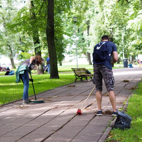 Sereikiškių parko pietinėje dalyje savanoriai šluoja pėsčiųjų taką. Kiti savanoriai grėbia vejoje susikaupusius medžių lapus.