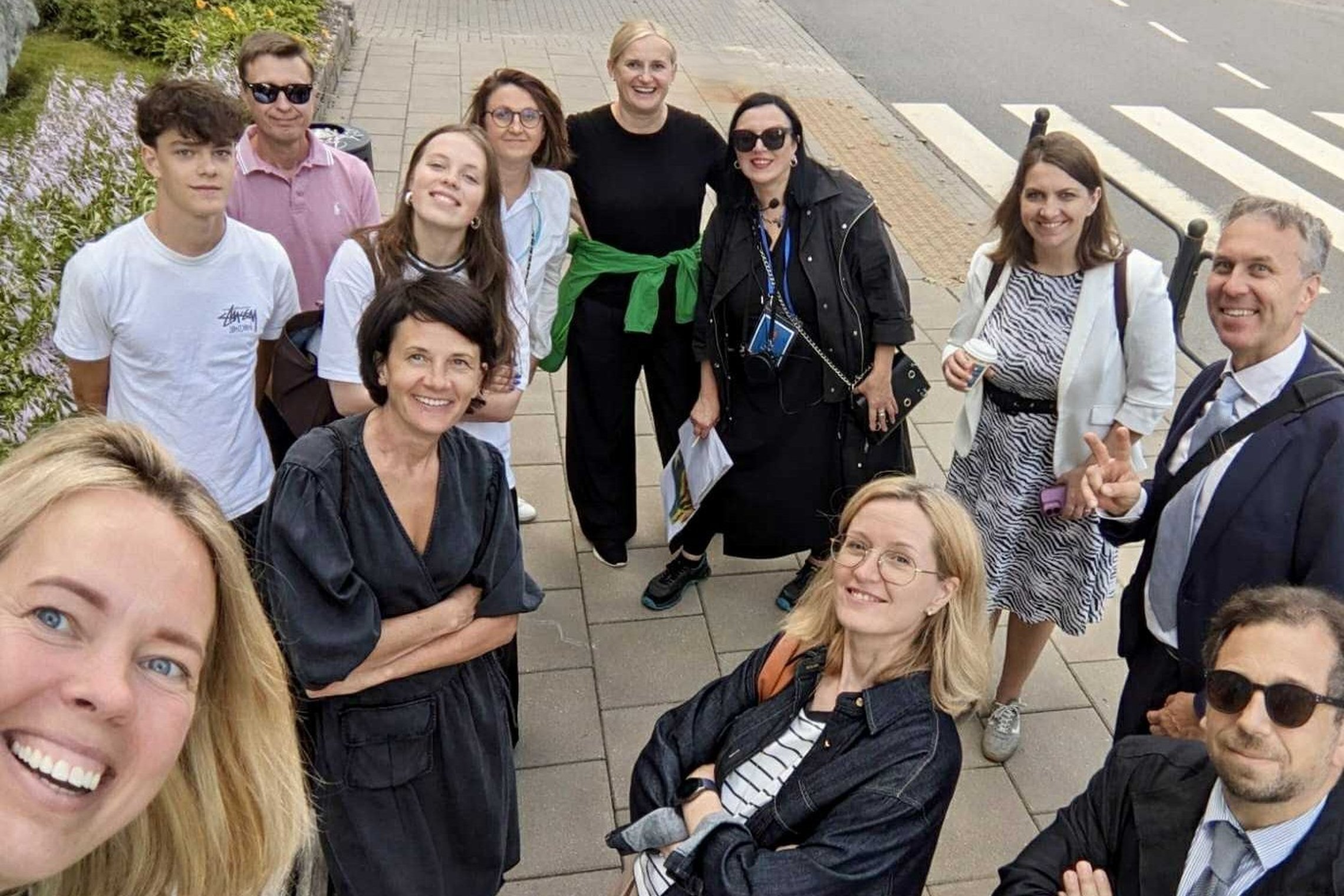 Nuotraukoje matomi 12 linksmai nusiteikusių žmonių – įvairaus amžiaus vyrai ir moterys, kai kurie su akiniais nuo saulės. Dauguma šypsosi ir žvelgia į kamerą.