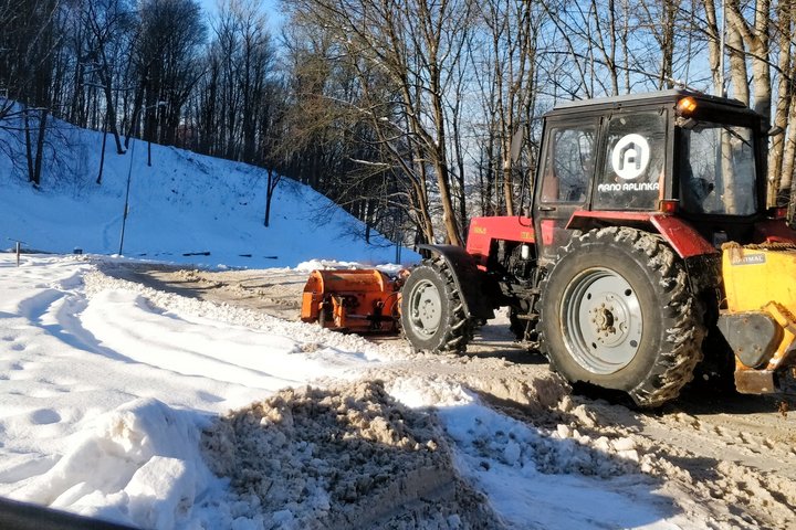 Traktorius nukasinėja įvažiavimą į mašinų stovėjimo aikštelę. Stumdo sniegą, barsto kelią smėliu. Giedra diena, žydras dangus, šalta.