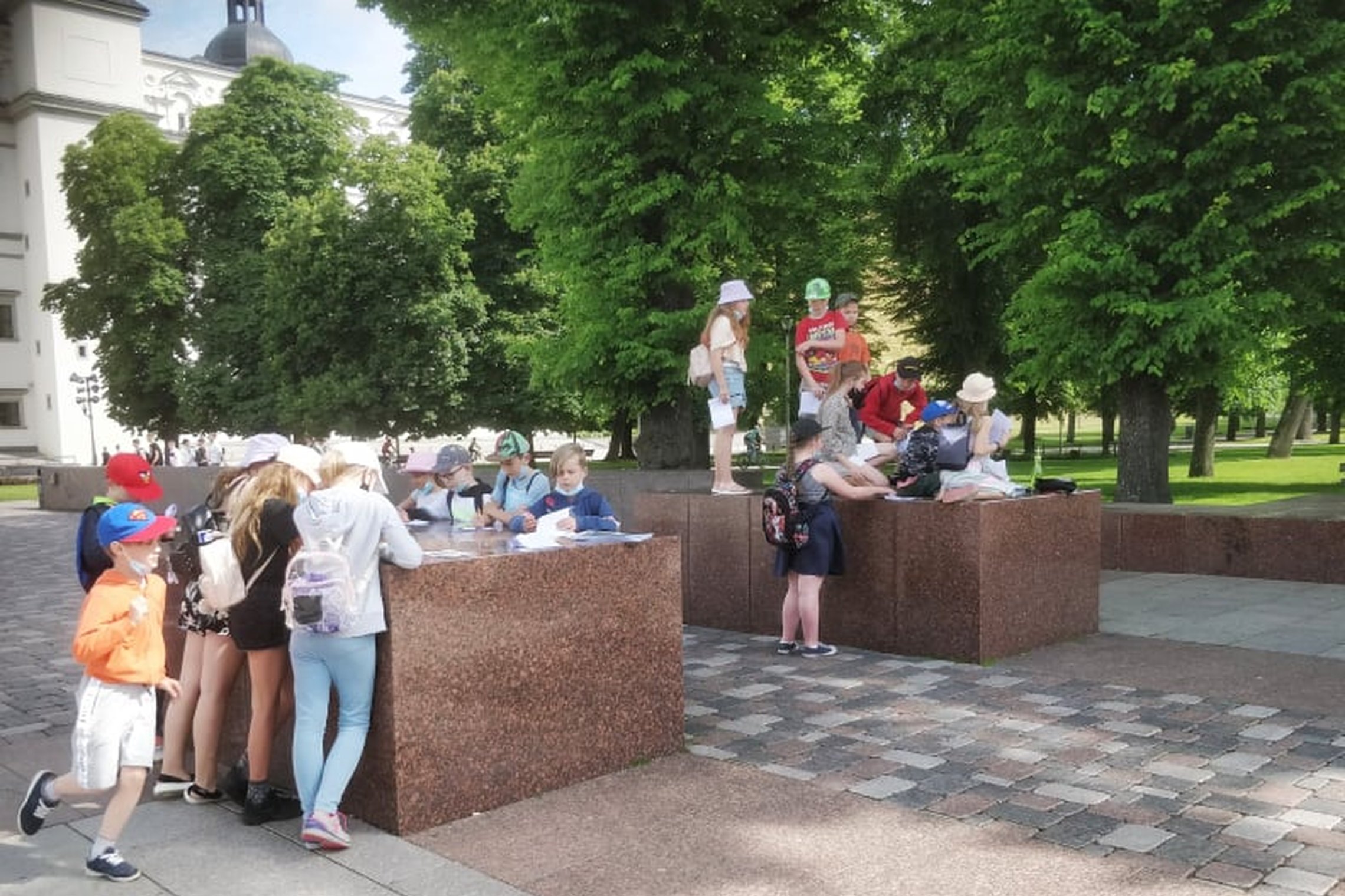 Grupė mokinių sprendžia užduotis ant granitinių blokų, kurie žymi buvusių Pilies vartų vietą.