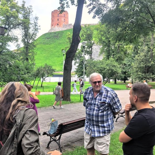 Grupė žmonių diskutuoja parke prie Gedimino kalno, fone – Gedimino pilies bokštas.