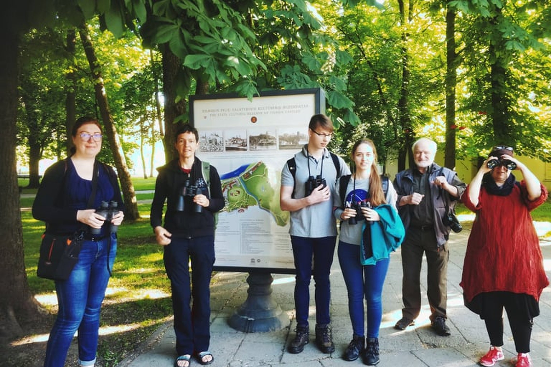 Grupelė žmonių stovi prie Vilniaus pilių rezervato stendo. Jie visi su žiūronais. Tai paukščių stebėjimo mėgėjai, išsiruošę gražų vasaros pradžios rytą stebėti paukščius Kreivosios piies teritorijoje (dabartinis Kalnų parkas).