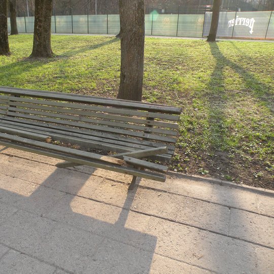 Sulaužytas suoliukas Pilių parke. Jis yra medinis ir iš kelių lentelių. Kelios lentos yra sulaužytos.