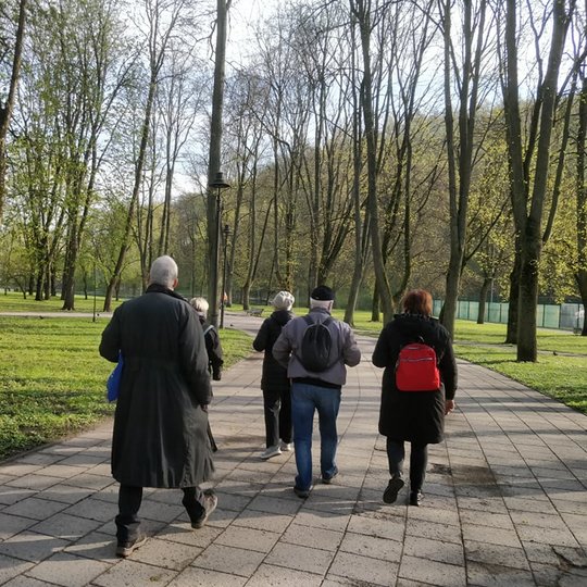 Nedidelė žmonių grupė eina parko taku. Ankstyvas pavasaris, visur šviežia žaluma.