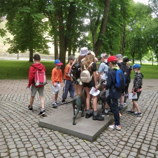 Grupė mokinių būriuojasi prie lietuvių skalikų skulptūrų Pilių parke.