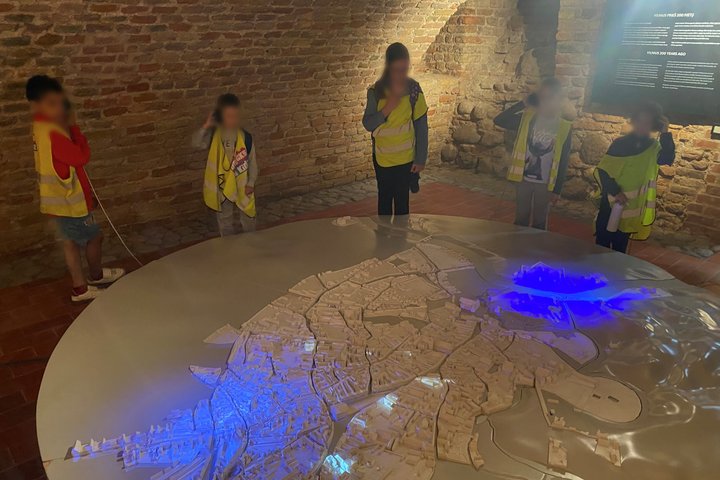 Vaikai su „Bricks4Kids“ stovyklos liemenėmis apžiūri apšviestą Vilniaus maketą Pilininko namo rūsyje