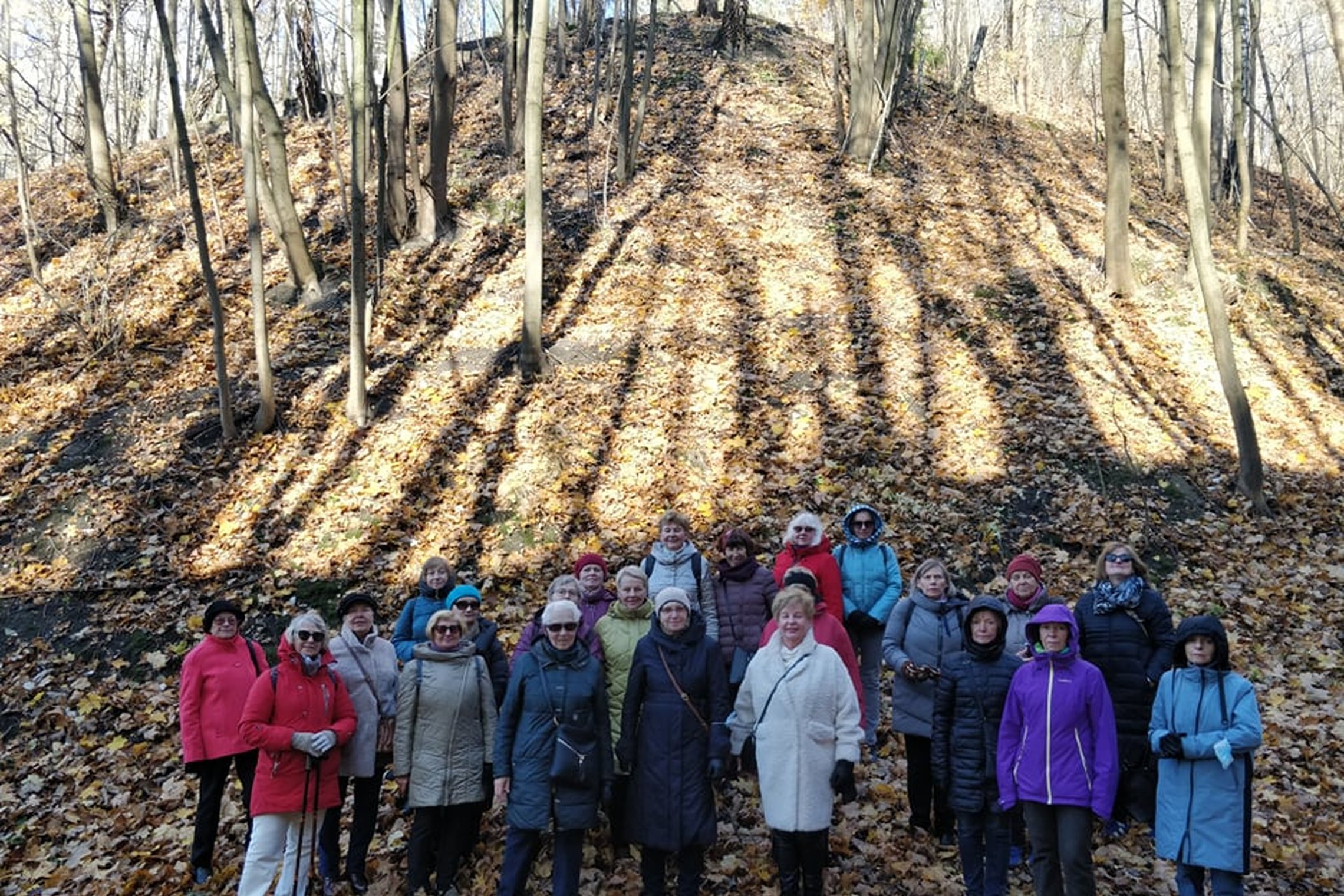 Ekskursijų dalyviai pozuoja nuotraukoje Didžiojoje griovoje. Saulėta rudens diena, lapai nuo medžių jau nukritę ant žemės.