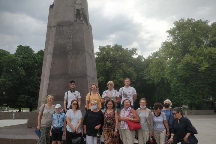 Didelė eksursijos grupė susirinkusi pozuoja Gedimino paminklo papėdėjė. Nors vasara, tačiau tamsi, debesuota diena.